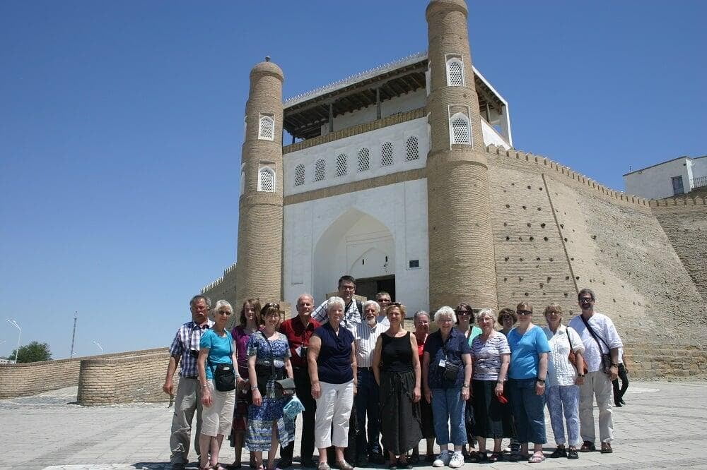 A group of tourists standing in front of The Ark, an ancient fortress in Bukhara, Uzbekistan, on a sunny day.