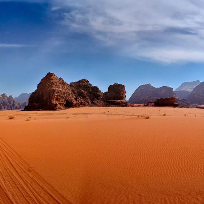 the Wadi Rum desert in Jordan, with expansive sandy terrain and rugged rock formations under a clear blue sky