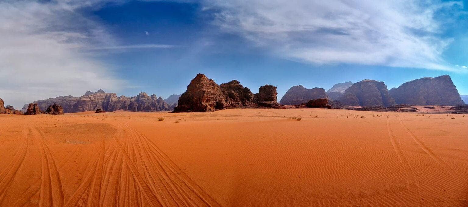 the Wadi Rum desert in Jordan, with expansive sandy terrain and rugged rock formations under a clear blue sky