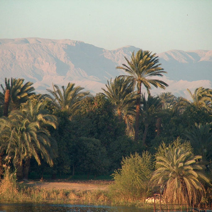 the Nile River in Egypt, with calm waters reflecting the surrounding greenery and distant hills under a partly cloudy sky