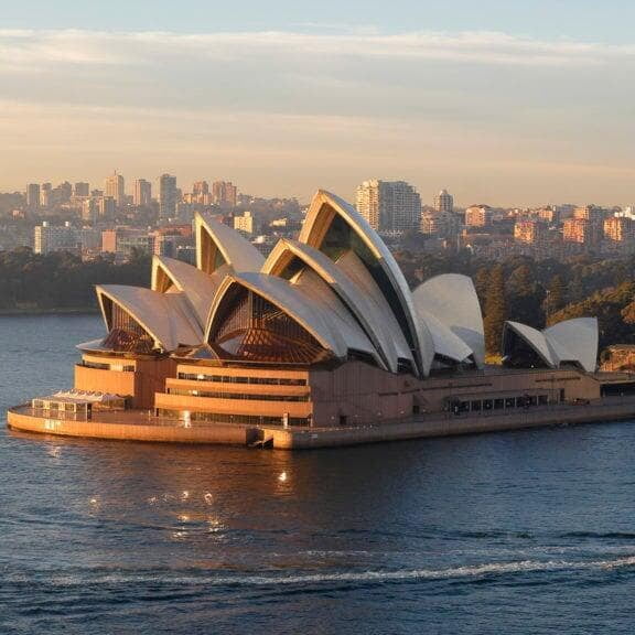 the Sydney Opera House with its distinctive sails, set against the vibrant backdrop of Sydney Harbour and a clear blue sky