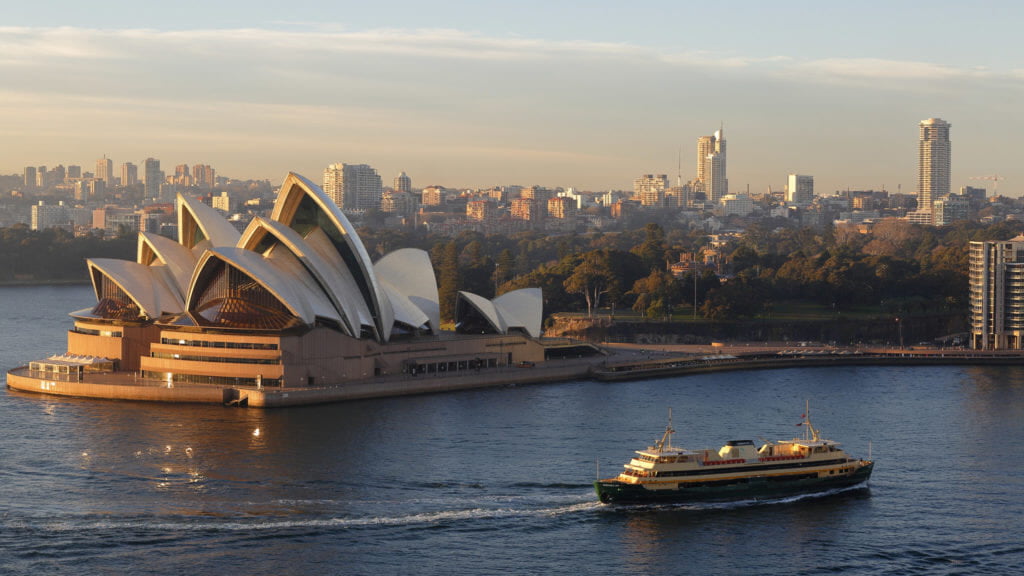 the Sydney Opera House with its distinctive sails, set against the vibrant backdrop of Sydney Harbour and a clear blue sky