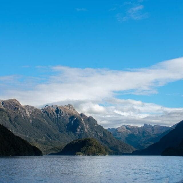 Lake Manapouri in New Zealand, with its tranquil waters reflecting surrounding mountains and a partly cloudy sky