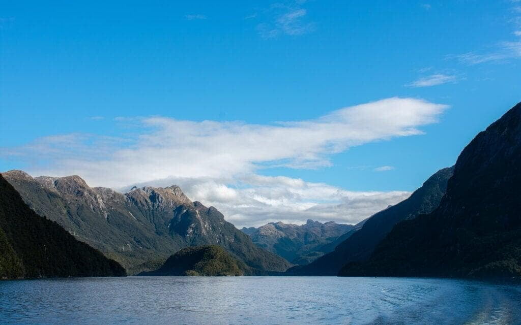 Lake Manapouri in New Zealand, with its tranquil waters reflecting surrounding mountains and a partly cloudy sky