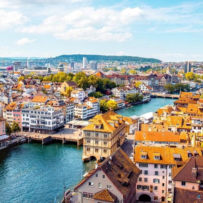 a scenic view of Zurich, Switzerland, with the cityscape and a prominent church steeple visible against a clear sky